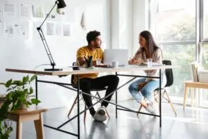 Two people sitting in front of a computer talking - AccessAlly Two people sitting in front of a computer talking