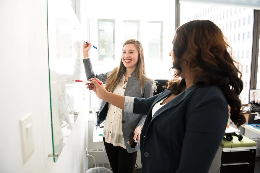 A woman coaching another woman in front of a dry-erase board