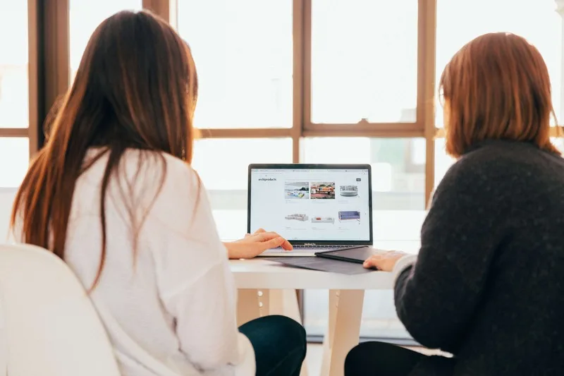 Two businesswomen talking and looking at a laptop.